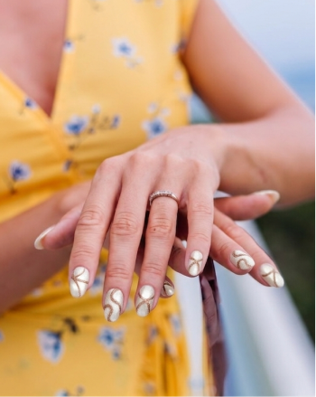 Close-up of a person's hands with decorative nail art wearing a yellow floral dress.