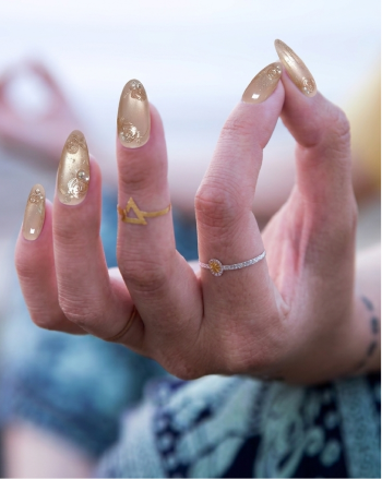 Close-up of a hand with gold nail polish and rings on a blurred background