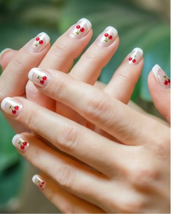 Close-up of hands with nail art featuring red berries and green leaves.