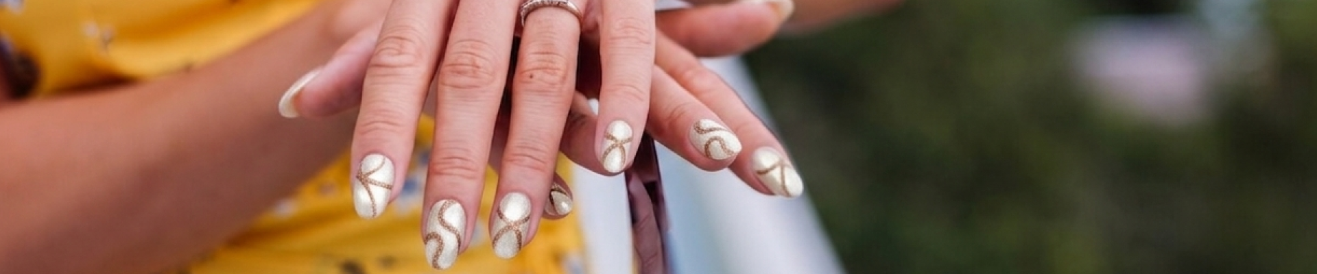 Close-up of hands with gold and white nail design against a blurred background